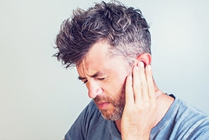 Boulder, Colorado man holds ear indicating TMJ disorder.
