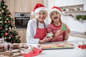 happy senior woman standing in kitchen with her granddaughter holding baked cookies and laughing 300x200 1