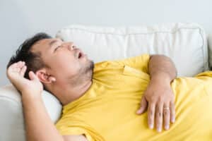 A man in a yellow shirt lying on a couch and snoring