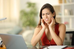 Woman at her work desk holding jaw in pain needing TMJ specialist in Boulder, CO