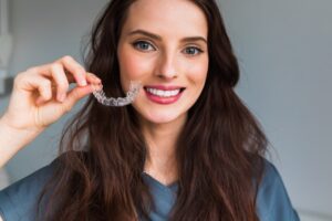 Woman smiling holding her Invisalign tray in Boulder, CO