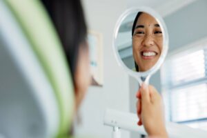 Happy woman looking in the mirror at her perfect smile after gum recontouring in Boulder, CO